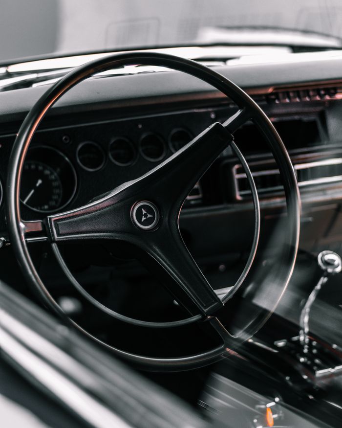 Through glass of old timer automobile with black round steering wheel and speedometer on dashboard parked on street in city